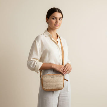 Woman holding a woven crossbody bag against a plain background